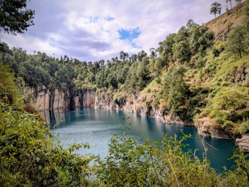 Un lac turquoise entouré de falaises et de végétation luxuriante sous un ciel nuageux.