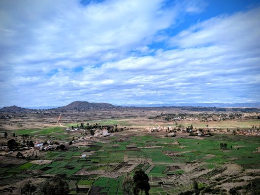 Paysage rural avec des champs verdoyants, collines au loin et ciel nuageux.